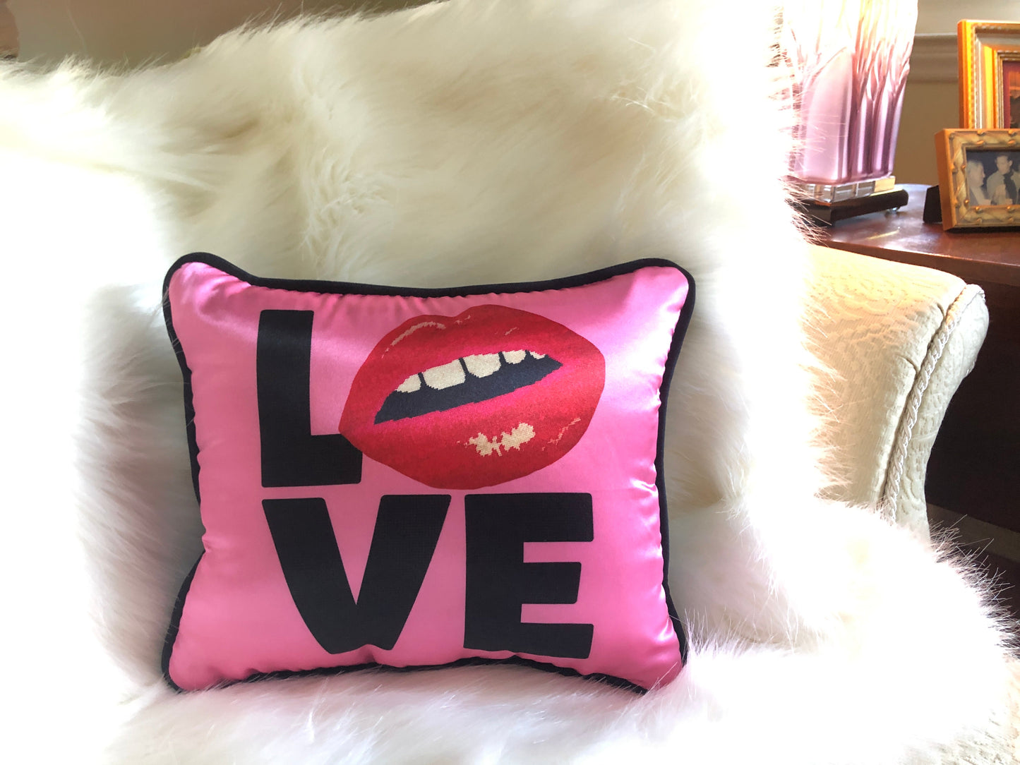 hot pink pillow with blackletters - L, red lips for an O, V & E stacked underneath. Shown on white faux fur throw.