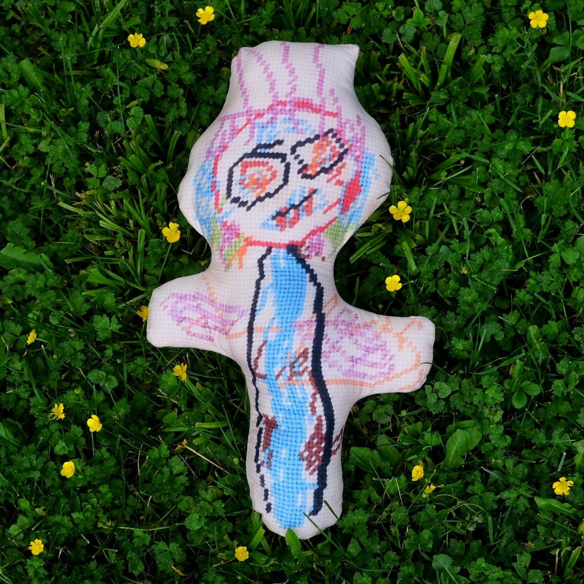 sculpted, colorful abstract monster with big eyes & wild hair laying on grass with yellow flowers