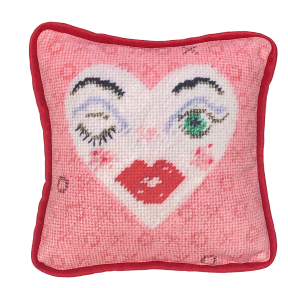 white heart pillow with winking eye and green eye, full lips, pink background with X and O