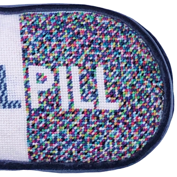 sculpted pill shape pillow is one-half white with blue letters and one half dotted, colorful pattern with PILL written in white