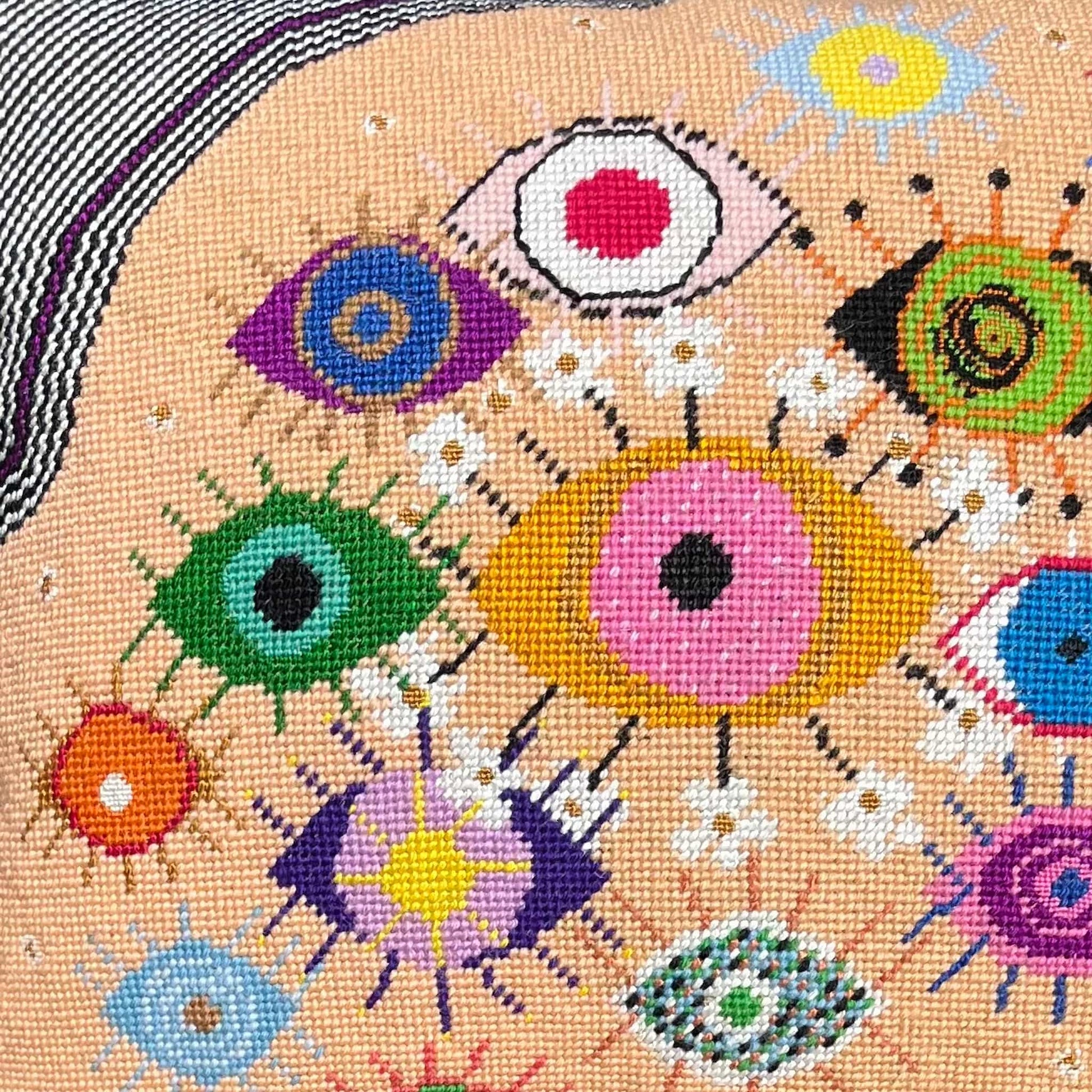 hand-embroidered lyrical pillow is covered in whimsical eyes of varying colors; vertigo band white swirl border
