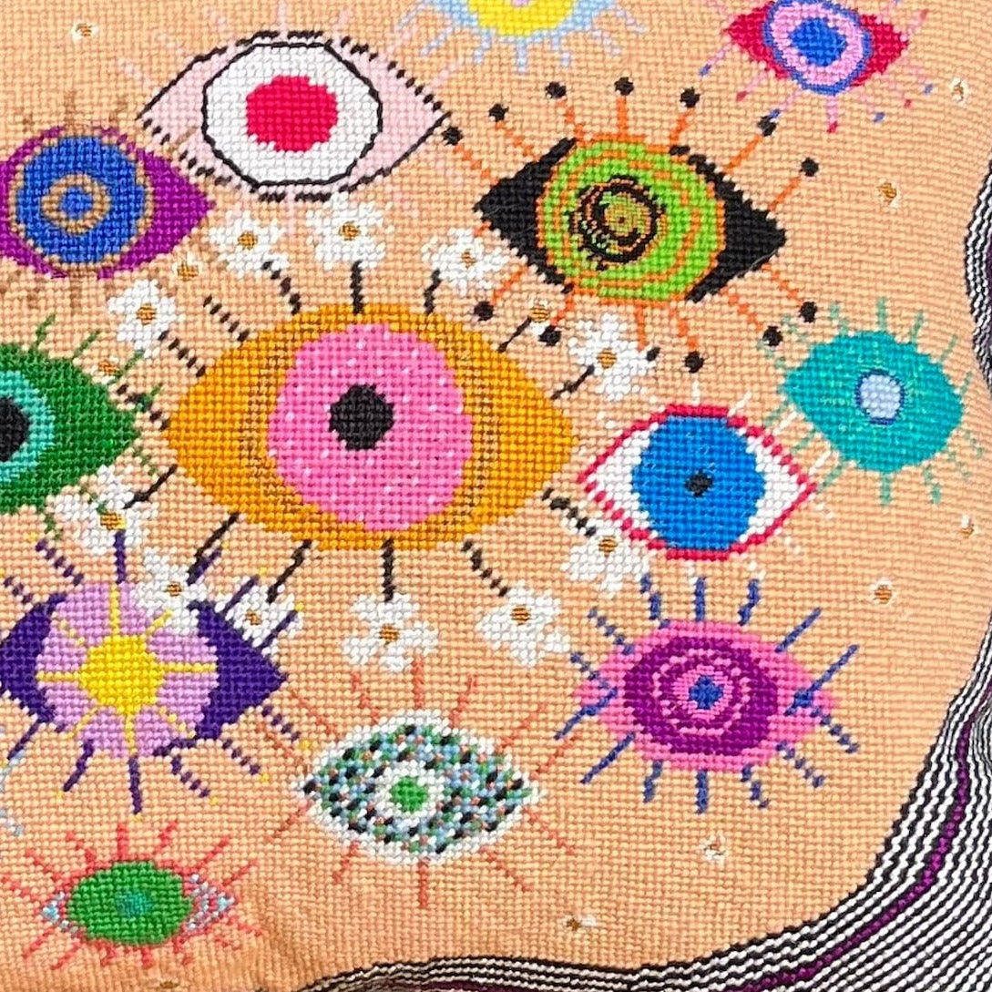 hand-embroidered lyrical pillow is covered in whimsical eyes of varying colors; vertigo band white swirl border
