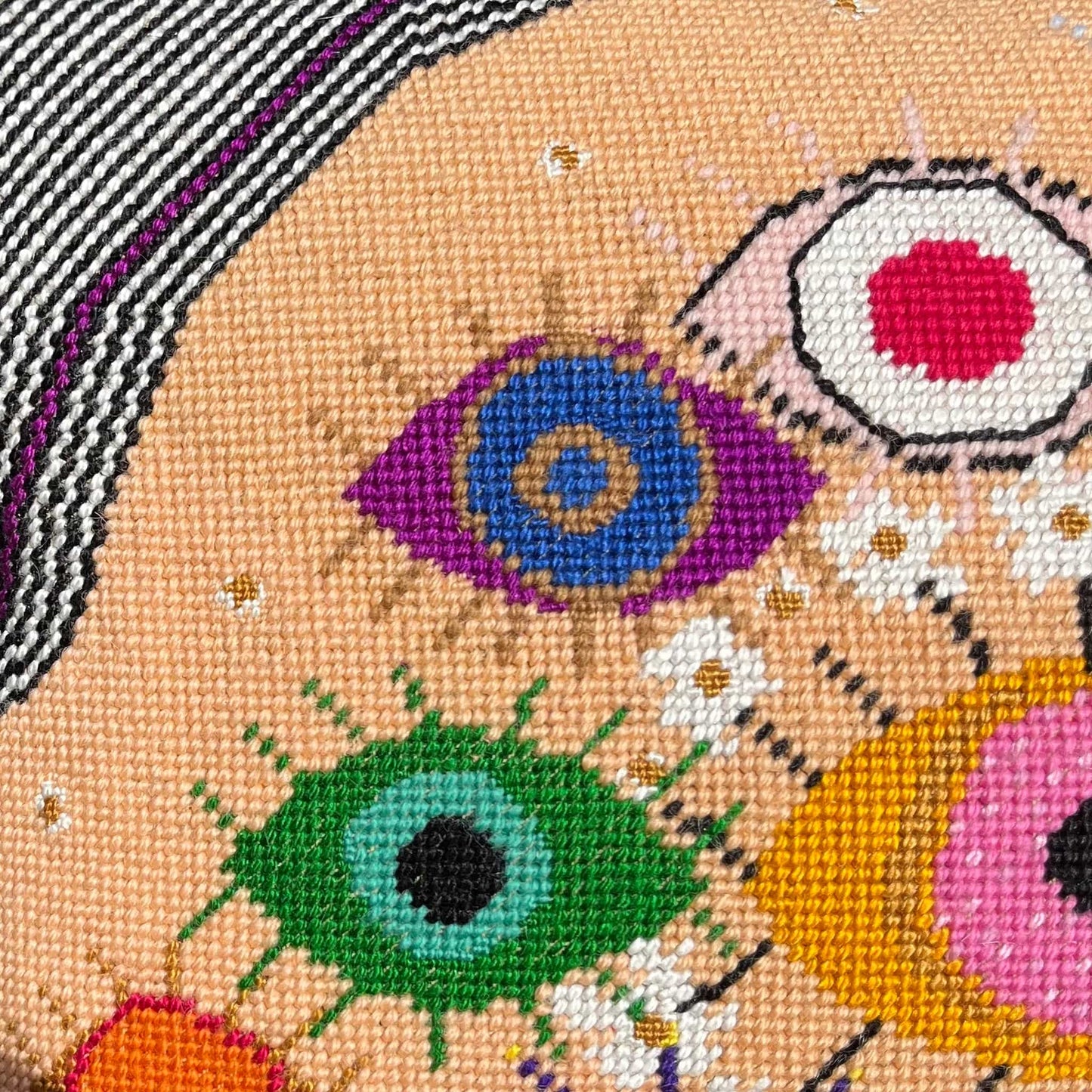 hand-embroidered lyrical pillow is covered in whimsical eyes of varying colors; vertigo band white swirl border