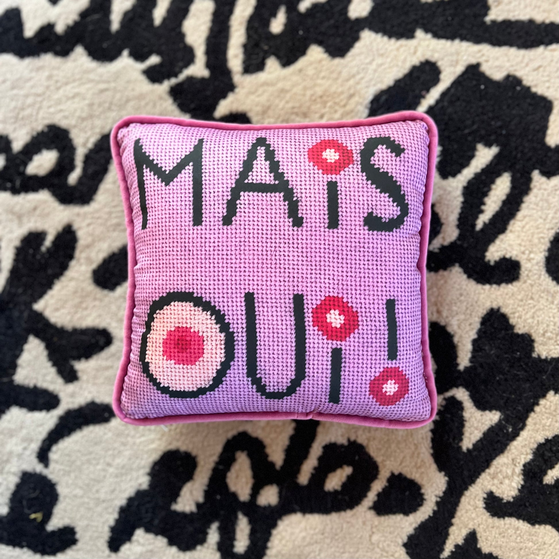 mais oui black stacked text with I dot and O that have cream colored centers with pink circles. Lavender pink background