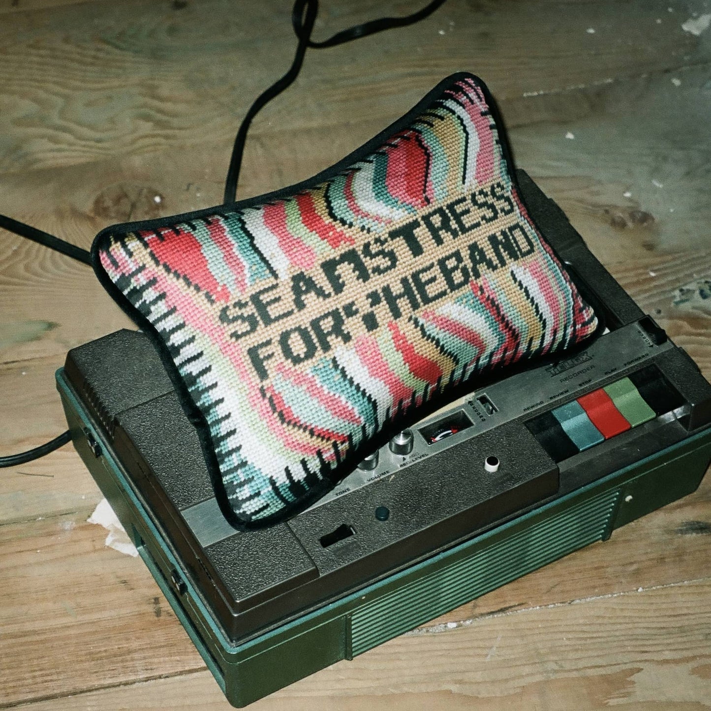SEAMSTRESS FOR THE BAND black letters inside tan box, surrounded by wavy bands of turquoise, pink, red, white, lime and a keyboard border
