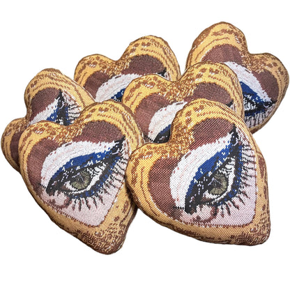 Mommani Threads x Haricot Vert "Heartfelt Glimpse" pillow is shaped like a heart and features a sultry green eye inside a gold frame.