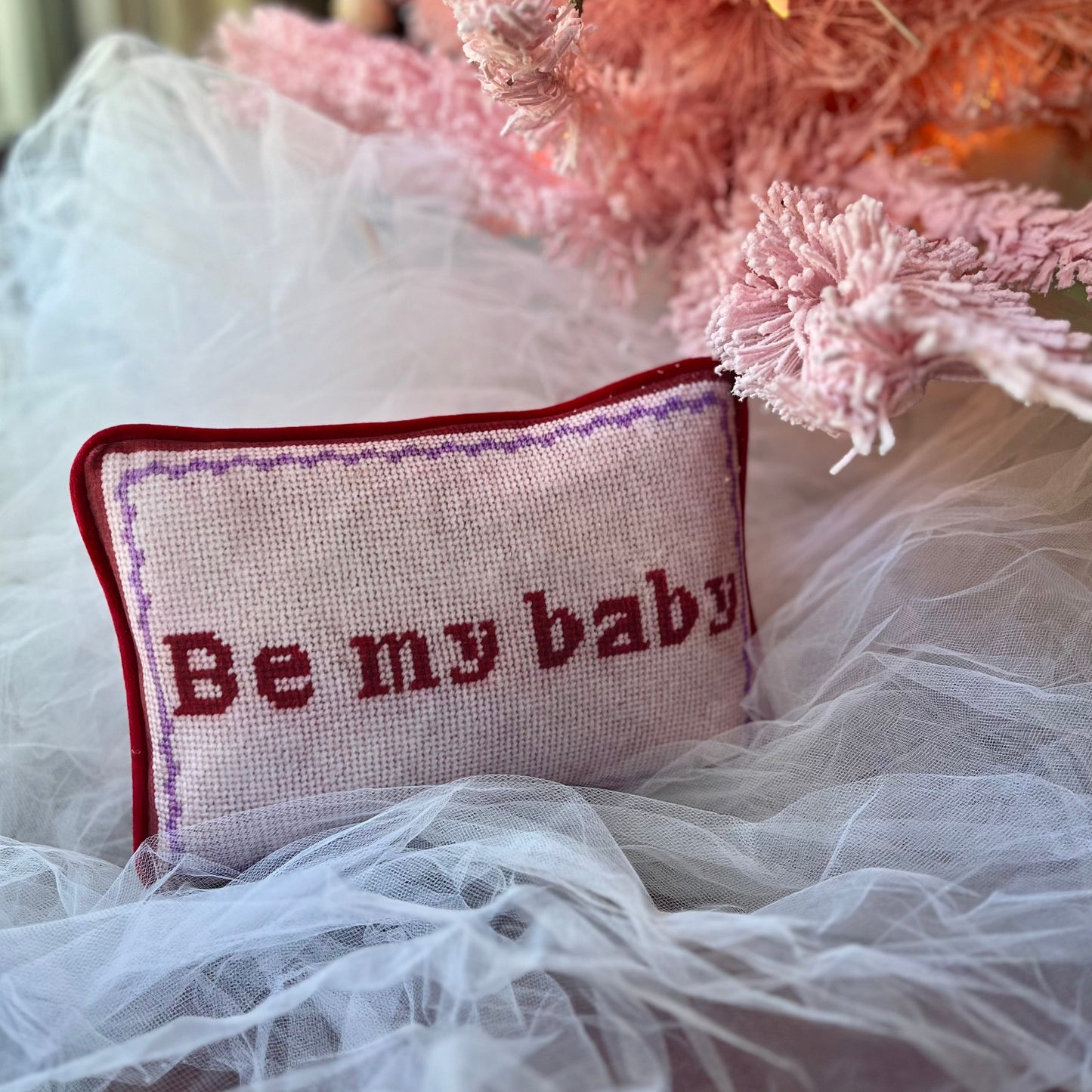 Pink velvet pillow with red letters that say "Be My Baby"; lavender wavy border.
