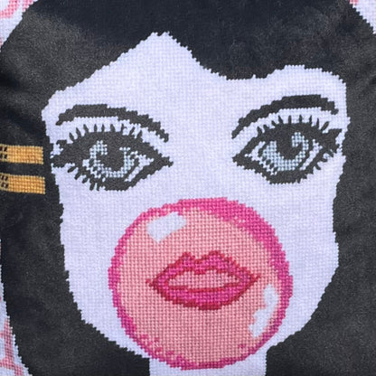 velvet pillow of doe-eyed girl with Jackie O hair and yellow hair clamp, blowing a bubble
