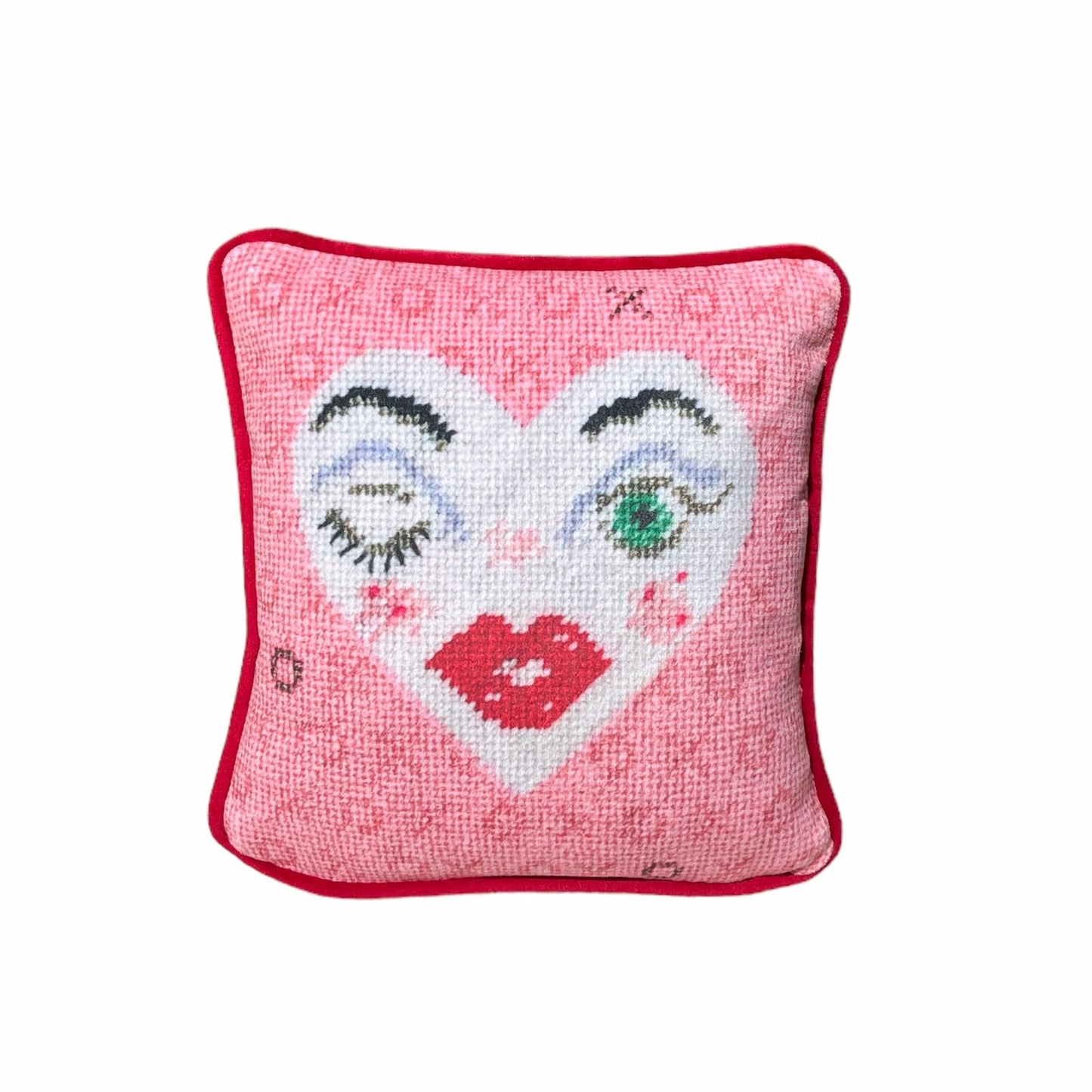 white heart pillow with winking eye and green eye, full lips, pink background with X and O