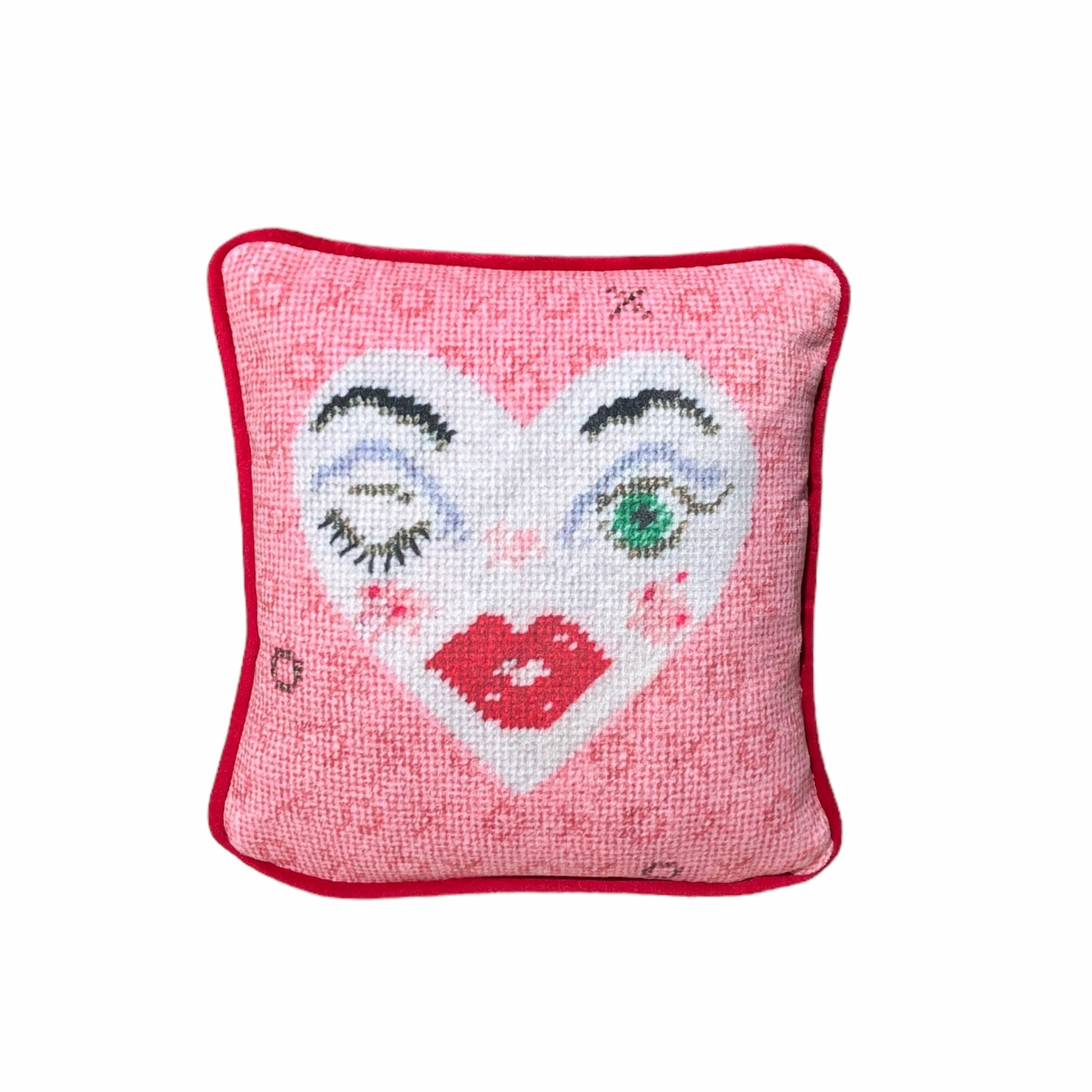 white heart pillow with winking eye and green eye, full lips, pink background with X and O