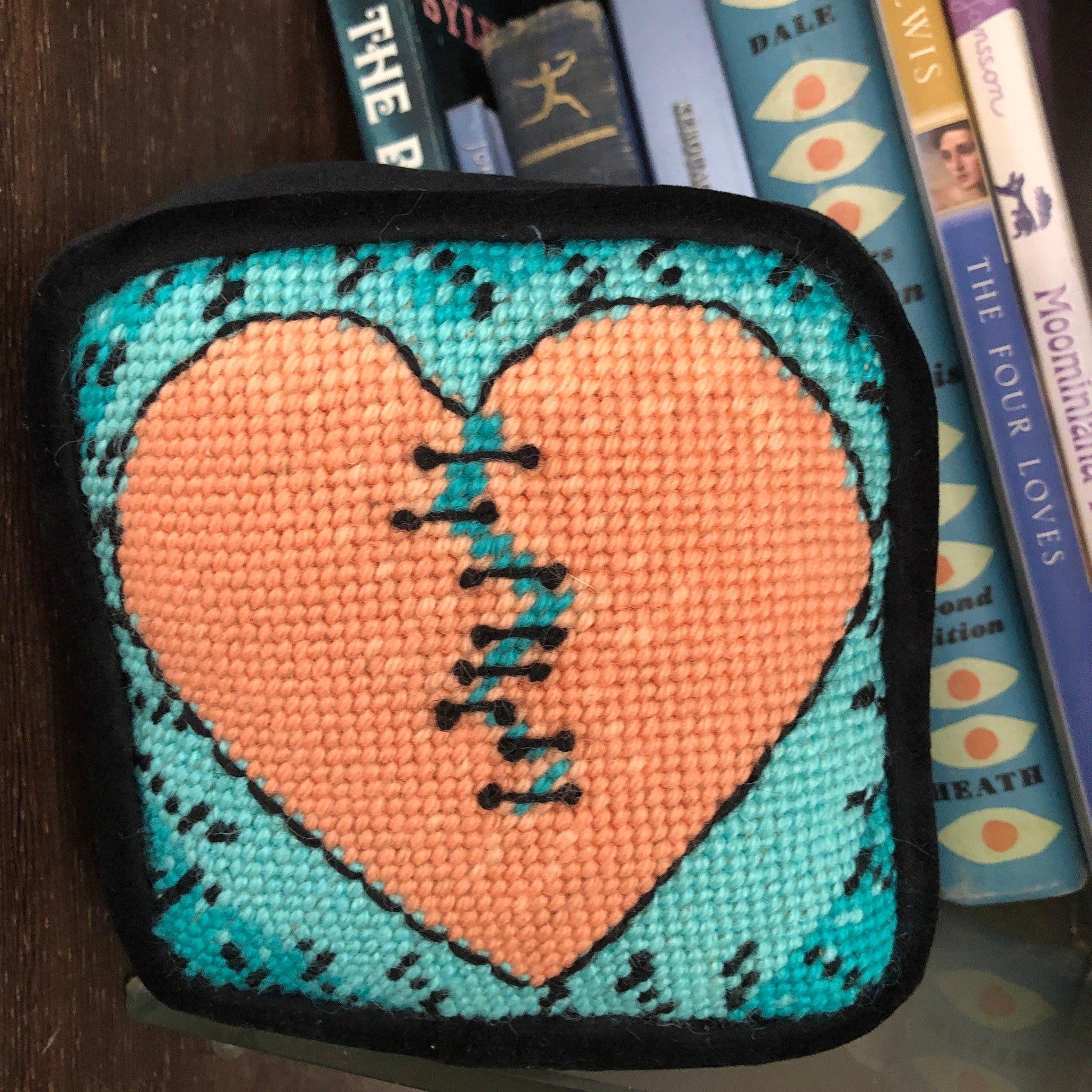 Variegated orange broken-heart pillow with turquoise background, book shelf