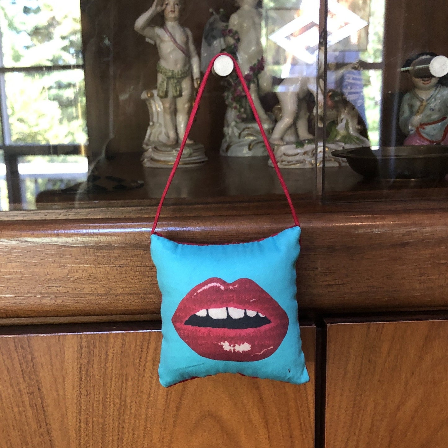 puffed pillow square ornament full red lips with open mouth and gapped teeth on turquoise background hanging on modern cabinet knob