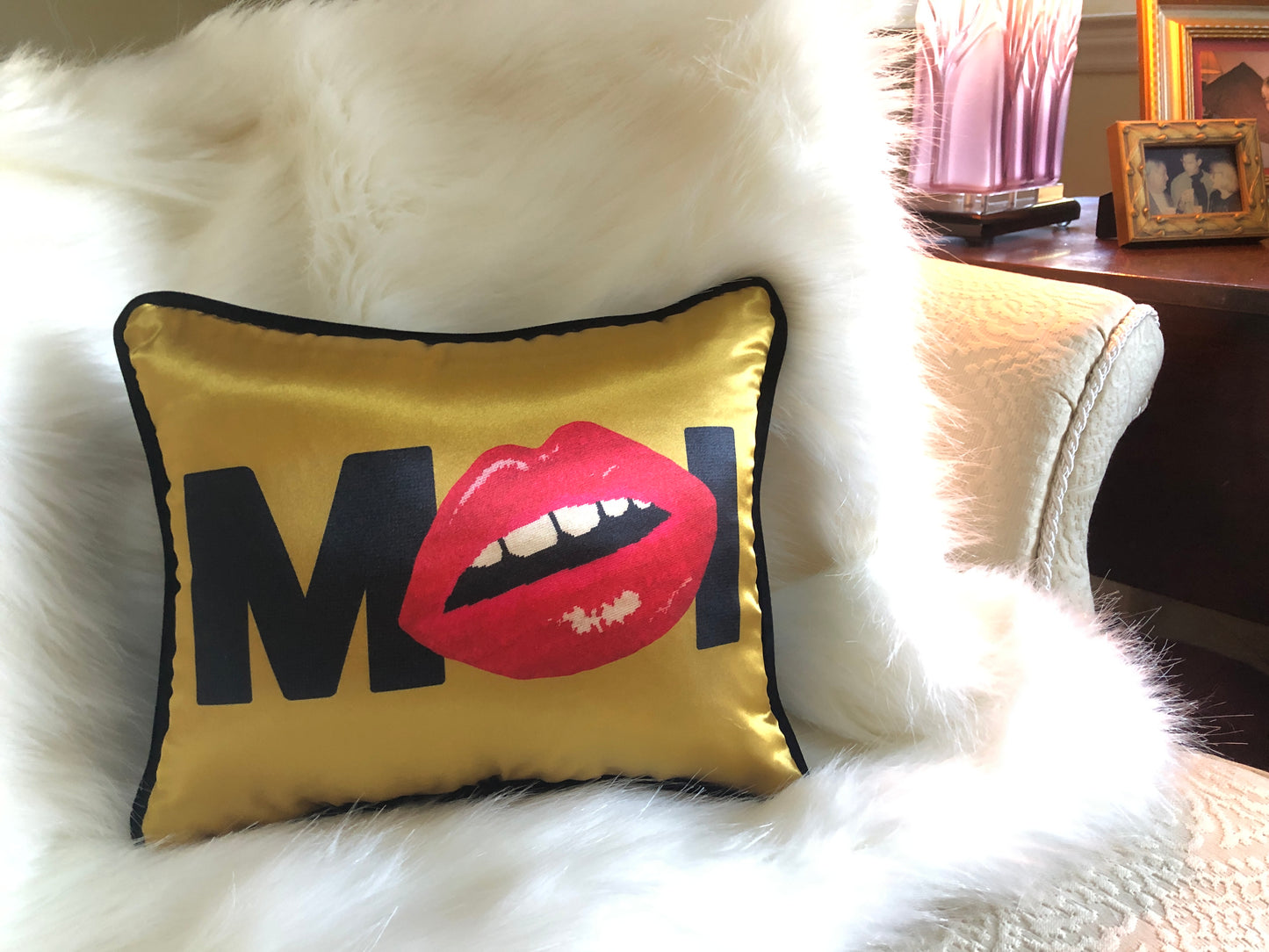 gold satin pillow with MOI written in black, red lips replacing the O. Shown on white faux fur throw.