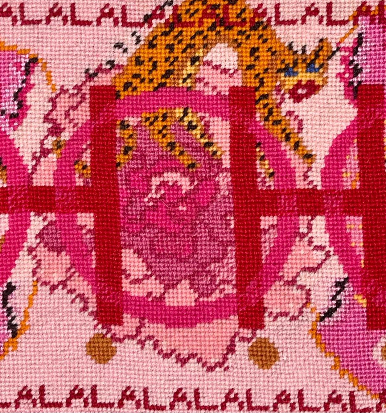 needlepoint pillow with pink and red colorful pattern, blue eye, cheetah, heart snakes, roses and lettering OOH in center with a LA LA LA border