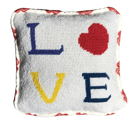 needlepoint pillow with white background, purple L, red heart, yellow V under the L and blue E, finished in white velvet with red lips pattern