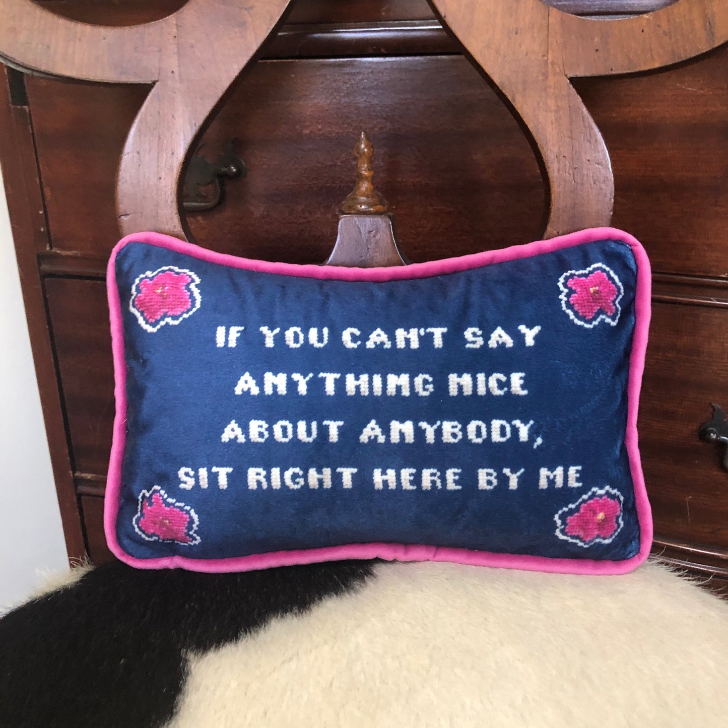 "If you can't say anything nice about anybody, sit right here by my" pillow with pink flowers in the corners and ink blue background.