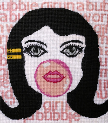 needlepoint big-eyed girl blowing pink bubble & hair flipped up, BUBBLE GIRL IN A BUBBLE GUM WORLD text behind image