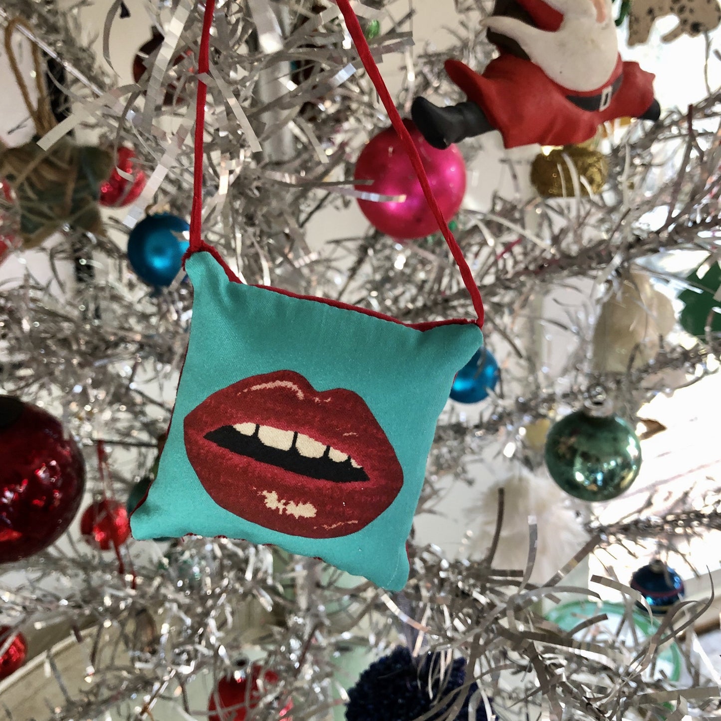 silver retro Christmas tree with puffed pillow square ornament full red lips with open mouth and gapped teeth on turquoise background