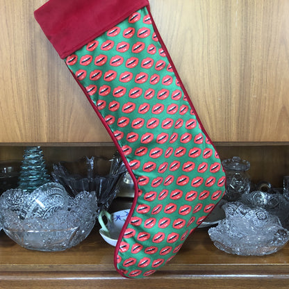 velvet holiday stocking covered in red lips with red cuff and hook, Christmas green background