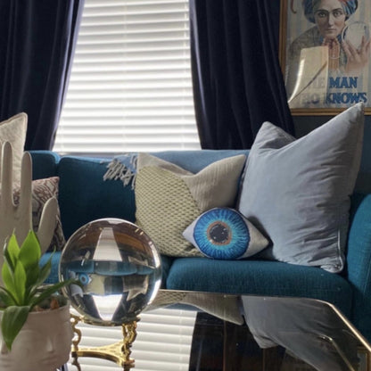 blue eye sculpted pillow on velvet couch, with palm art and globe