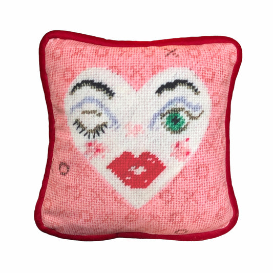 white heart pillow with winking eye and green eye, full lips, pink background with X and O
