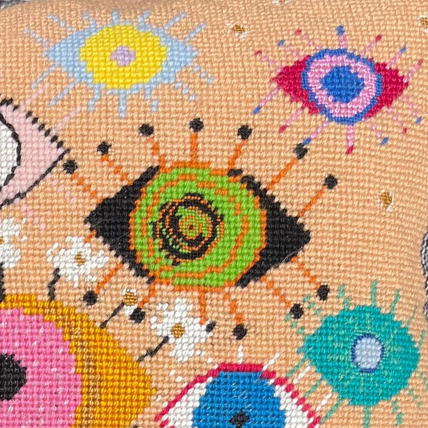 hand-embroidered lyrical pillow is covered in whimsical eyes of varying colors; vertigo band white swirl border