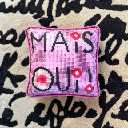 mais oui black stacked text with I dot and O that have cream colored centers with pink circles. Lavender pink background