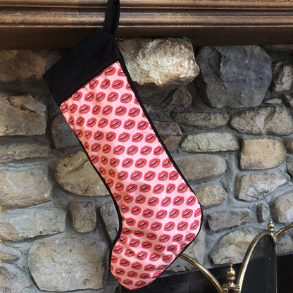 velvet holiday stocking covered in red lips with black cuff and hook, pink background fireplace