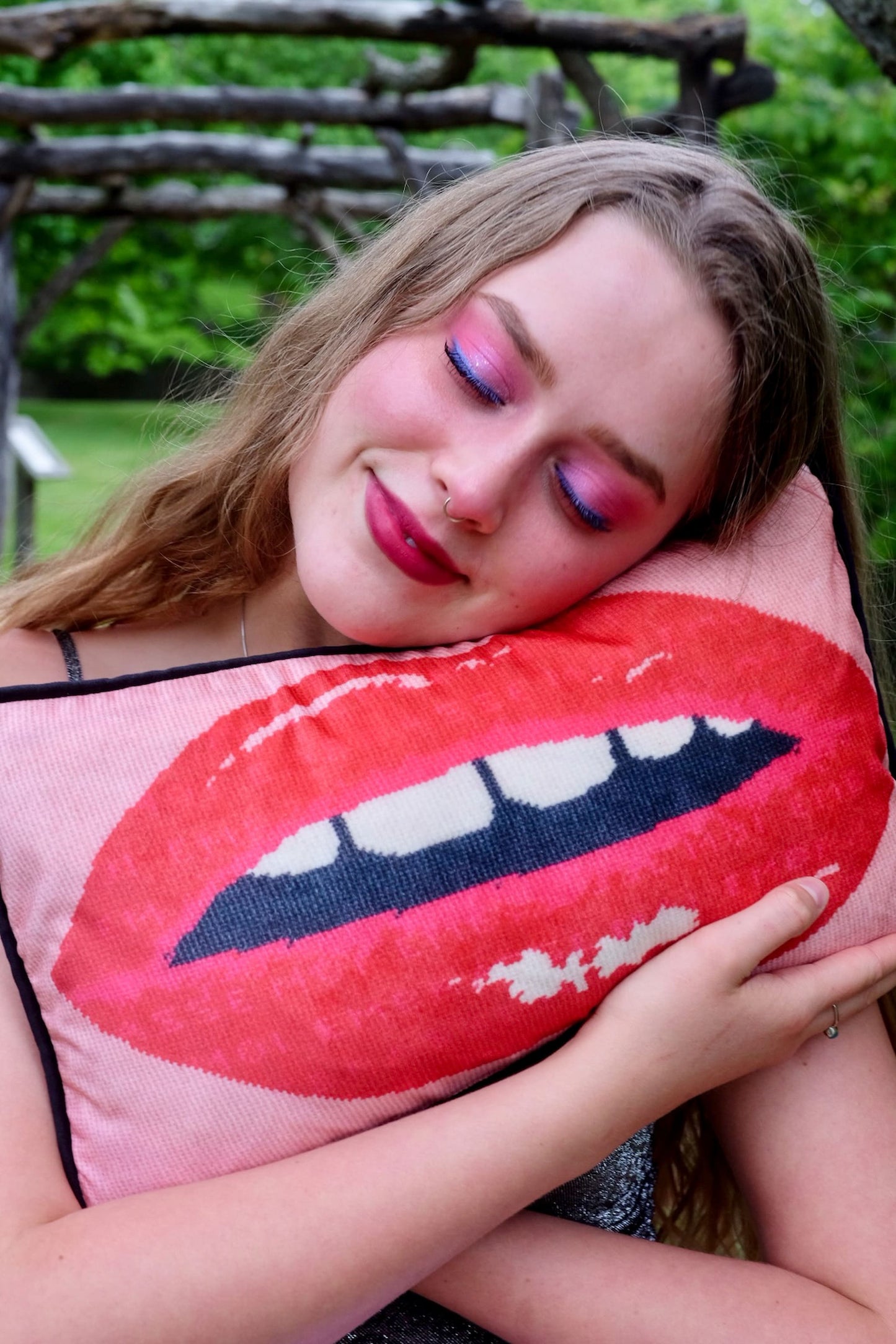 beautiful blonde model holds pink velvet pillow with red lips with open mouth and gapped teeth