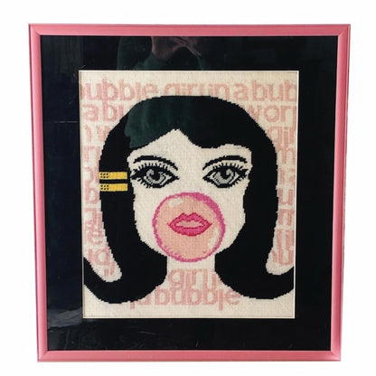 needlepoint big-eyed girl blowing pink bubble & hair flipped up, BUBBLE GIRL IN A BUBBLE GUM WORLD text behind image