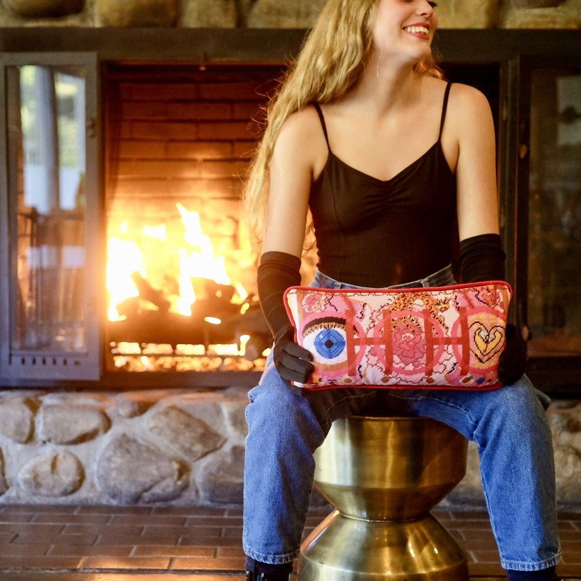 velvet pillow with pink and red colorful pattern, blue eye, cheetah, heart snakes, roses and lettering OOH in center with a LA LA LA border model at fireplace