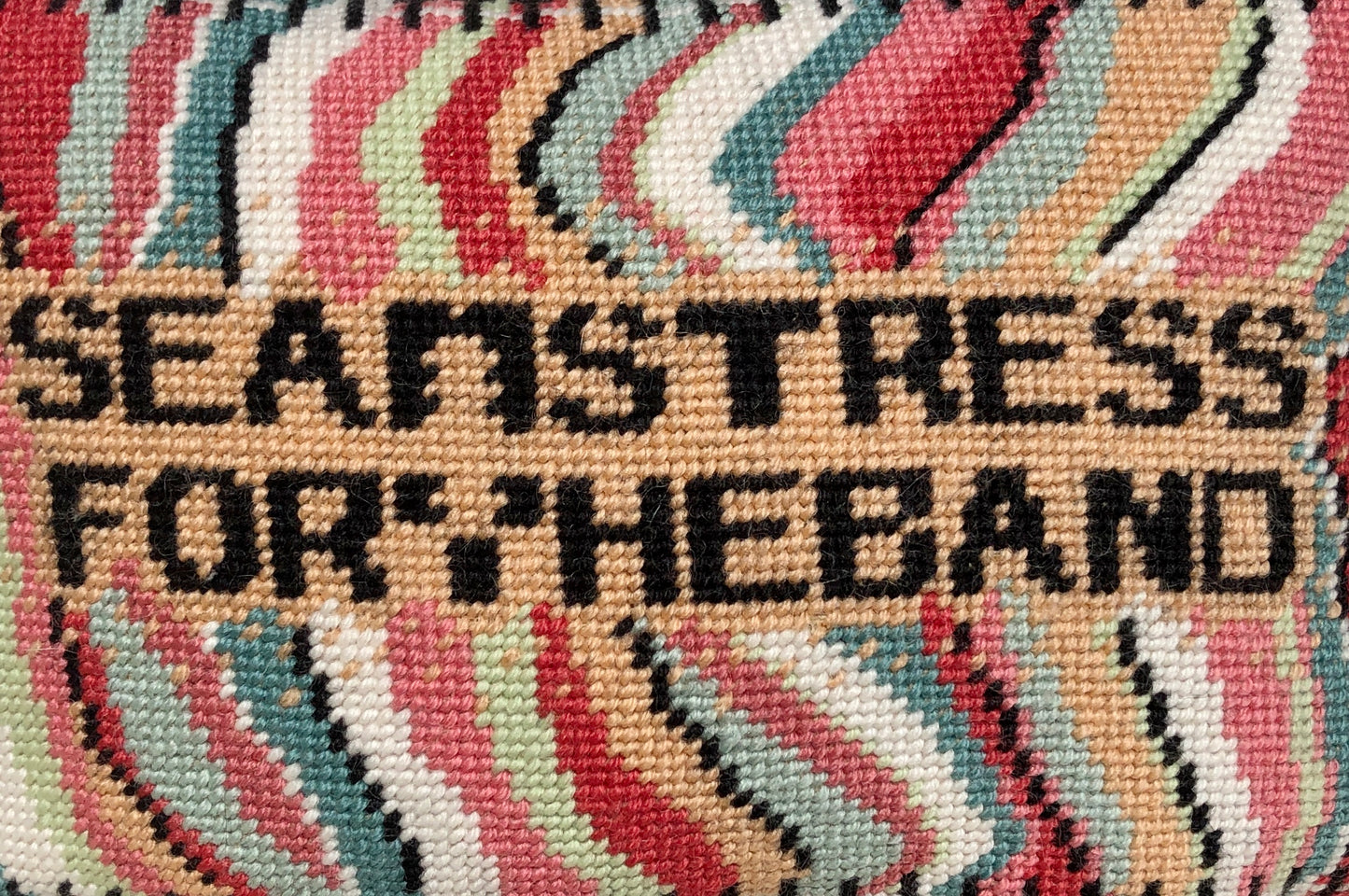 SEAMSTRESS FOR THE BAND stitched in black inside tan box, surrounded by wavy bands of turquoise, pink, red, white, lime and a keyboard border